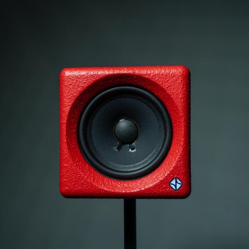 A compact cube studio monitor with a single full-range driver photographed head on.