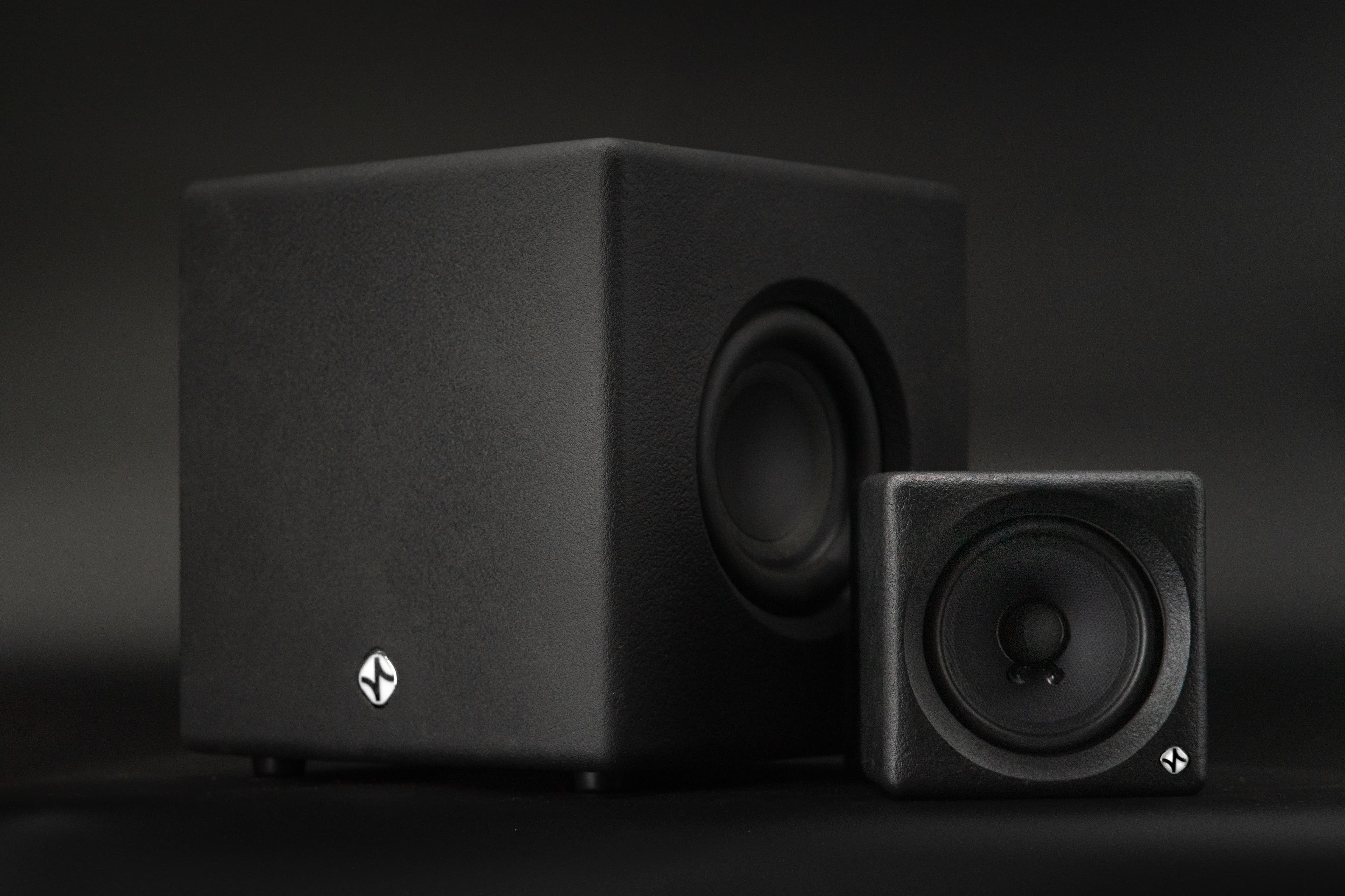 A sealed subwoofer cube and a small cube monitor photographed together against a dark background.
