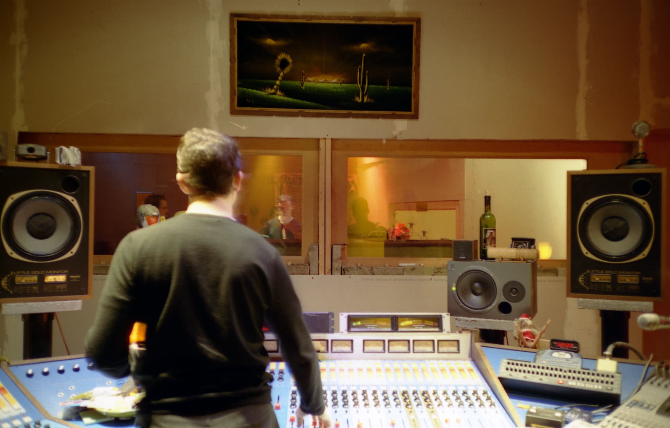 An engineer standing at a mixing console in a control room, with large monitors either side and nearfield monitors on the console bridge.