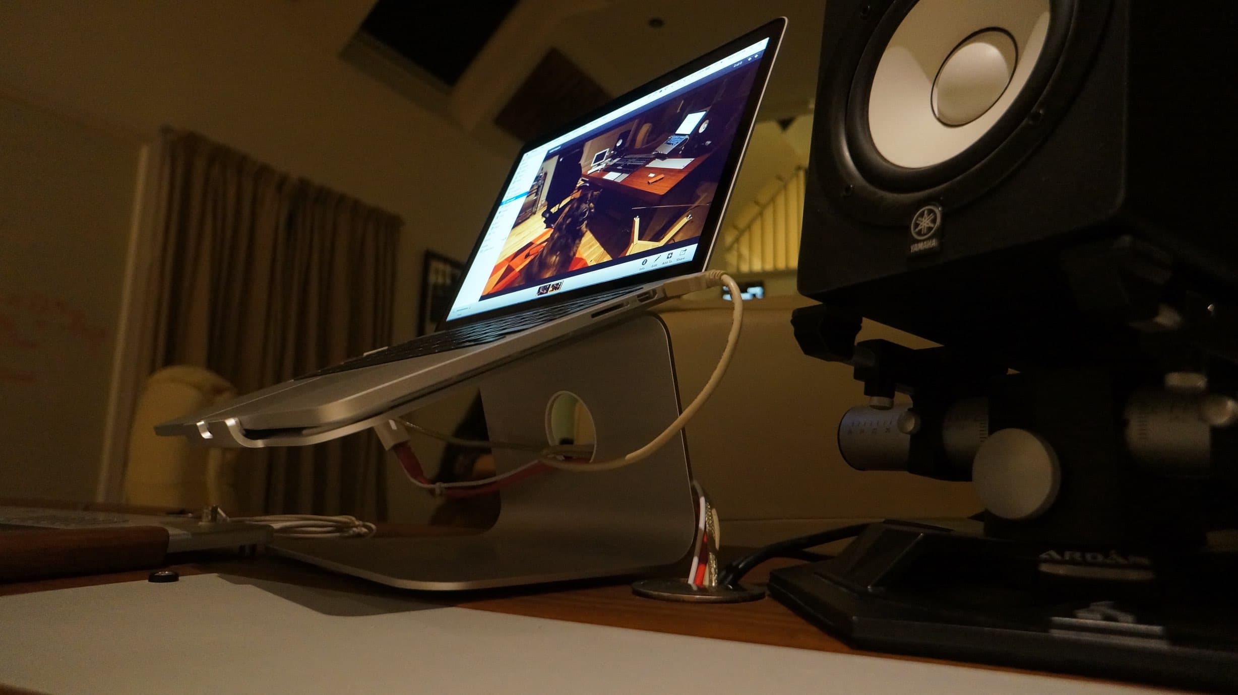 A desk with a laptop raised on a stand and a studio monitor raised on its own stand beside it.