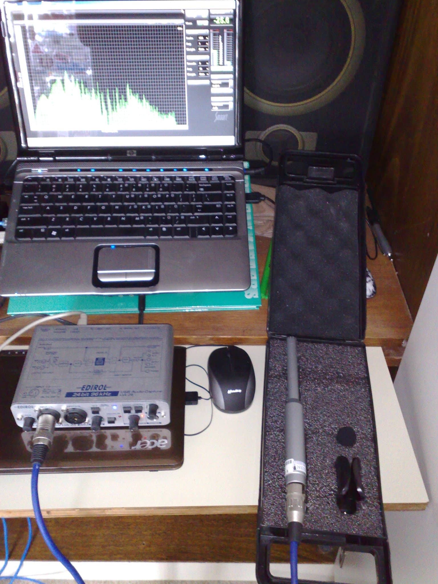 A laptop running audio analysis software next to a measurement microphone and an audio interface on a desk.