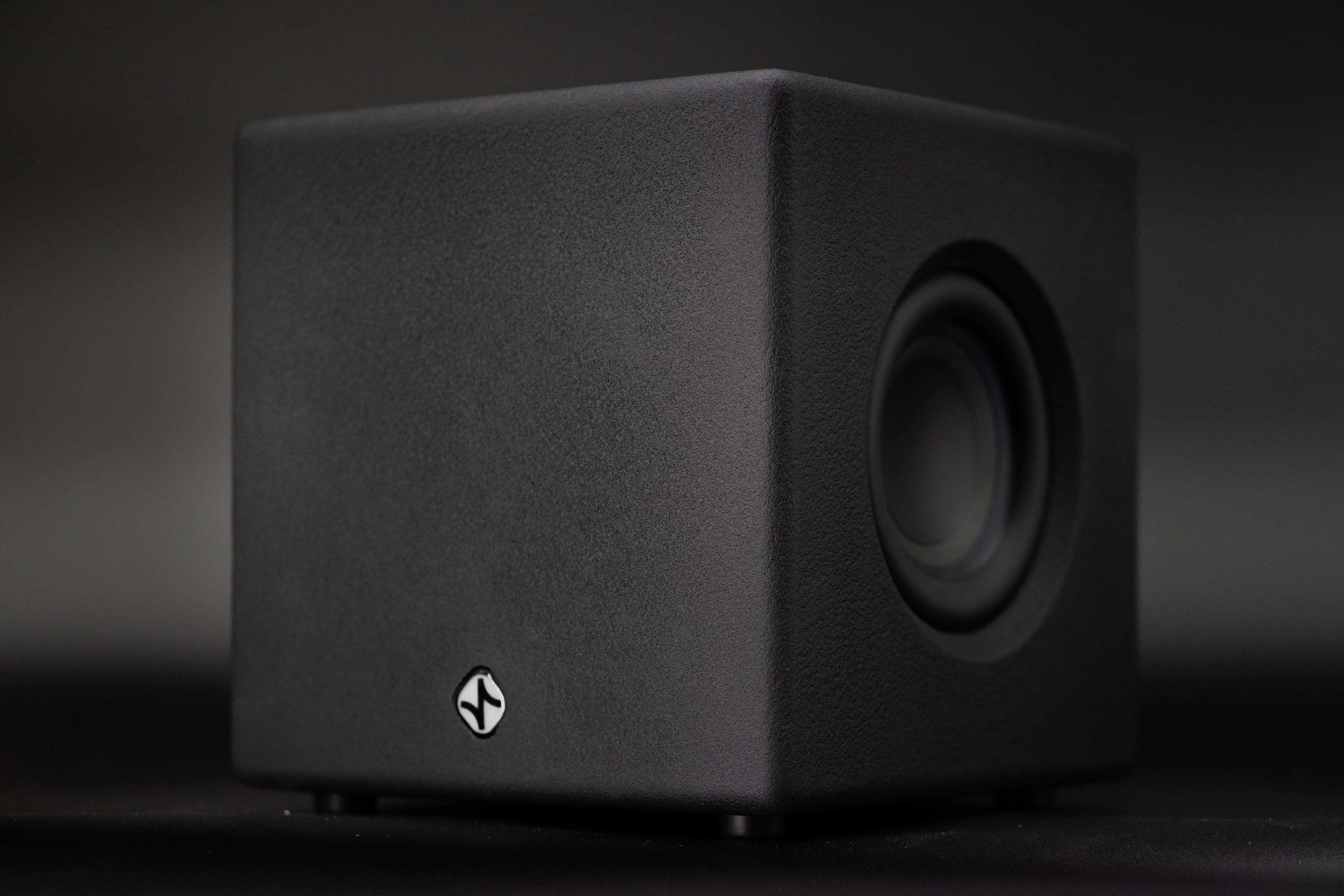 A sealed black subwoofer cube photographed at an angle against a dark background.
