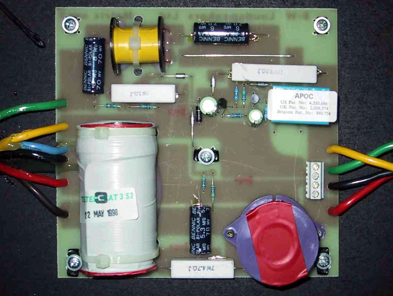 A passive loudspeaker crossover board carrying inductors, capacitors and wirewound resistors, with coloured wires leading off it.