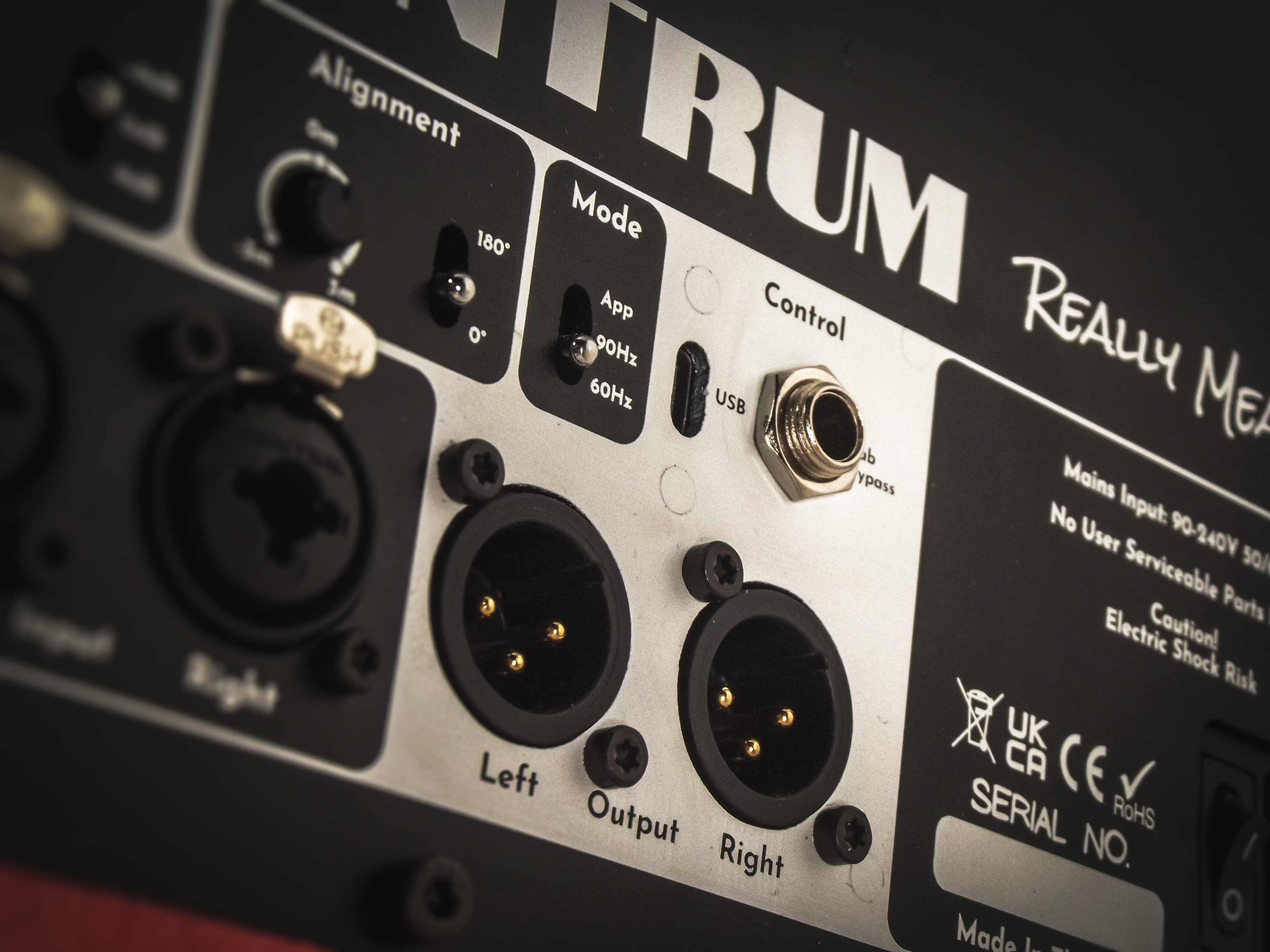 Close-up of the rear panel of an active monitor showing XLR inputs and outputs, alignment and mode switches, and mains input labelling.